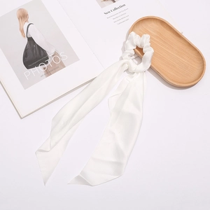 Detail of ivory satin scrunchie with long ribbons on elegant wooden tray setup