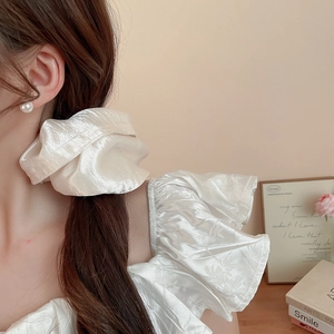 Close-up of a large French cream satin scrunchie showing glossy fabric texture and soft folds