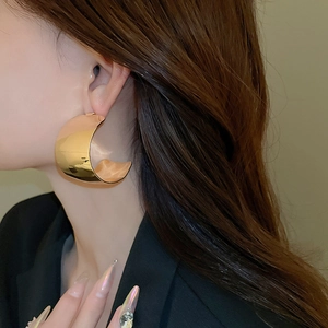 Close-up of a large gold polished C-shaped hoop earring worn by a female model