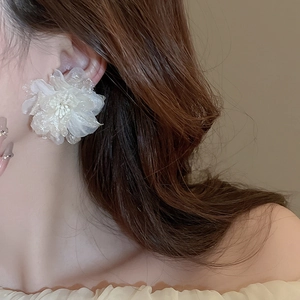 Close-up of a large white mesh flower earring on a model for an elegant bridal look