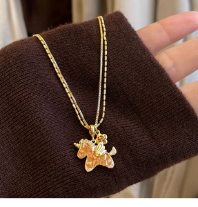 Detail of gold double-layered necklace with orange crystal unicorn and tiny crown pendant