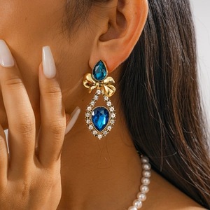 Close-up of vintage gold drop earrings with blue gemstones and a bow on model