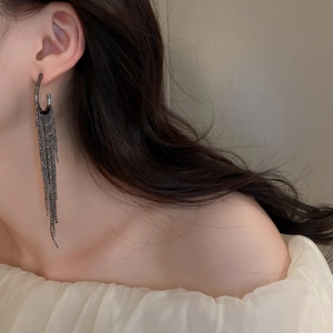 Detail of long black fringe tassel earring with C-shaped hoop on model shoulder