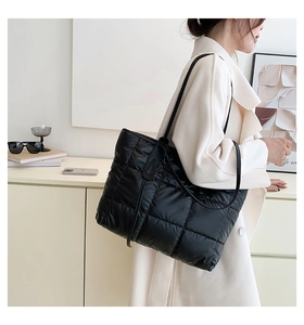 Detail view of large black quilted puffer tote bag shown on model in a soft indoor setting