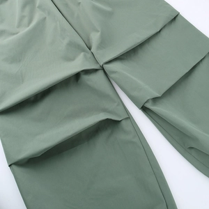 Dettaglio dei pantaloni cargo verdi con design a pieghe a tre strati e tessuto sintetico liscio