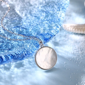 Macro shot of silver round pendant necklace with white shell inlay over blue water surface