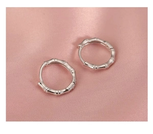 Detail shot of silver bamboo-textured huggie hoop earrings on smooth pink silk fabric