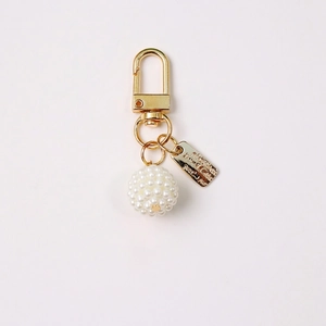 Detailed view of golden keychain with white pearl cluster and metallic brand tag charm