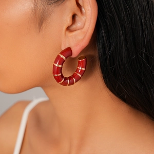 Detailed close-up of C-shaped red enamel earrings with golden stripes on a model