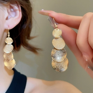 Close-up of matte gold sequin tassel earrings worn by a model against a beige background