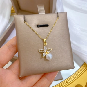 Detail of gold floral necklace with white zircons and a round pearl on a satin base