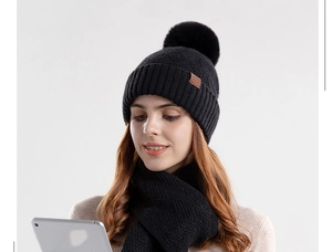 Detailed view of black knitted beanie with large faux fur pompom and scarf set