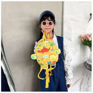 Toddler modeling a yellow dinosaur print backpack against a stylish studio wall background