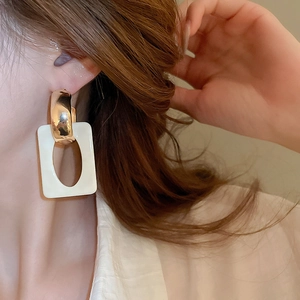 Detail of geometric resin earring with gold metal hoop and marbled white pendant
