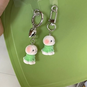 Close-up of white flocked bichon puppy keychain wearing a green shirt and pink ears