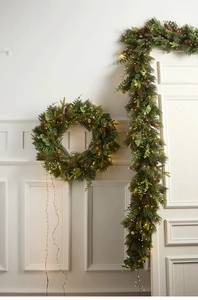 Close-up of PE Christmas garland and wreath with pine cones and warm LED string lights