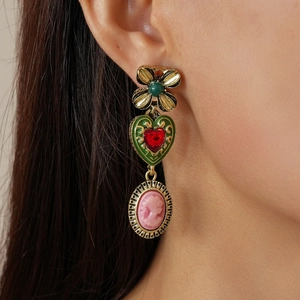 Macro shot of vintage gold earrings with heart green gems and relief portrait pendant