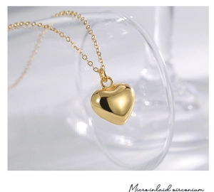 Macro shot of polished gold-plated heart pendant on a glass rim with fine chain