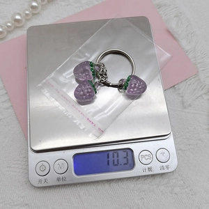 Detailed view of translucent purple strawberry keychain being weighed on a digital scale