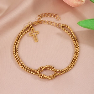 Close-up of gold layered chain bracelet with cross pendant on pink silk background