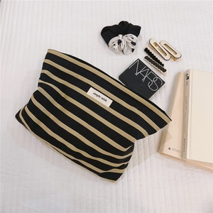Detailed view of a striped canvas makeup bag with a woven label on a lifestyle background