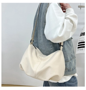 Side view of cream pleated dumpling crossbody bag on model with soft lighting detail