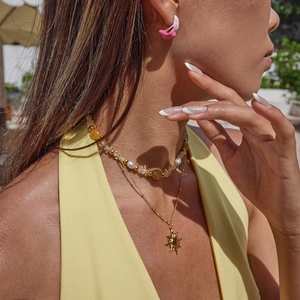 Detail of a layering necklace with golden sun pendant and pink floral petal earrings