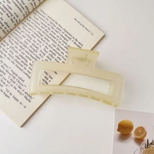 Gros plan d'une pince à cheveux rectangulaire crème mate sur un livre, style minimaliste