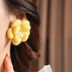 Gros plan de boucles d'oreilles fleurs en feutre jaune avec centre perlé sur un mannequin