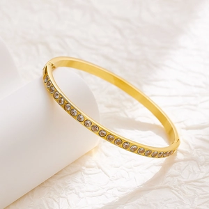 Elegant gold titanium steel hinged bangle with inset crystals on a white pedestal