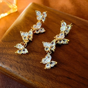 Macro shot of gold butterfly tassel earrings with sparkling crystals on dark wood
