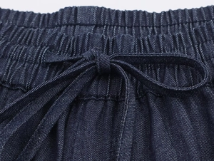 Detailed close-up of dark blue denim pants with elastic waistband and drawstring bow