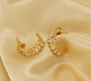 Close-up of gold C-shaped earrings with baguette-cut cubic zirconia on silk fabric