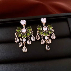 Macro view of gold teardrop tassel earrings with green and white zircon on black leather
