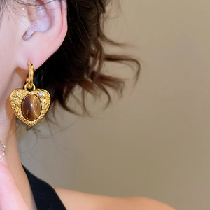 Detail of heart-shaped gold earring with tiger eye stone and crystal on model