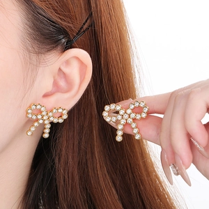 Close-up of 18K gold-plated bow earrings with shimmering pavé crystal details on a model