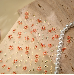 Detail of floral nail stickers with orange petals, gold leaves and 3D pearls