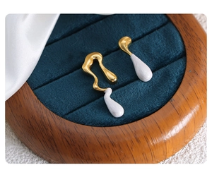 Macro shot of asymmetric gold teardrop earrings with white enamel on navy velvet display