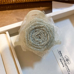 Dettaglio di un fermaglio bianco per capelli con fiore di rosa in pizzo blu chiaro