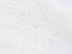 Detailed macro view of white poplin fabric featuring intricate floral embroidery and texture