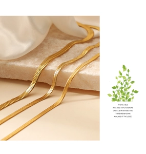 Detailed view of three golden 2-5mm flat snake chain necklaces on white marble and silk