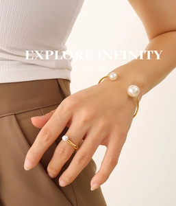 Detail view of gold-plated open bangle and pearl ring set on model in elegant outfit