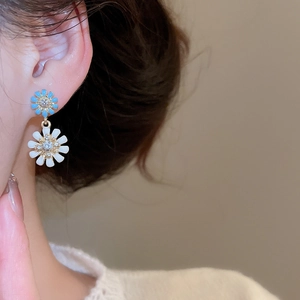 Detail view of double-layer daisy earrings with blue and white enamel petals and zircons