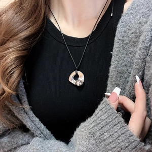 Close-up of silver irregular fluid ring pendant on black cord worn by a model