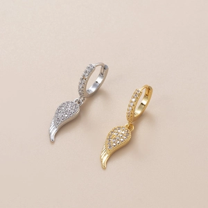 Macro view of gold and silver angel wing earrings with zircon stones on beige background
