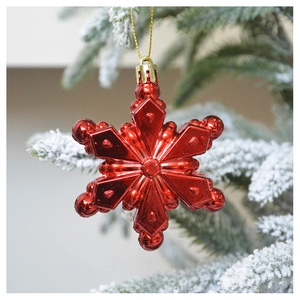 Close-up of a vibrant red snowflake ornament hanging on a snowy Christmas tree branch