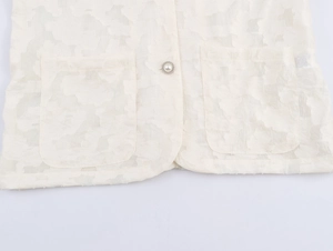 Détail du blazer en dentelle crème avec texture gaufrée, poches et bouton perle