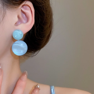 Close-up of light blue marble-textured resin ball drop earrings worn by a model