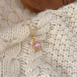 Close-up of gold necklace featuring an oval pink gemstone pendant on knit fabric