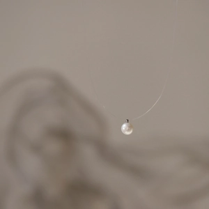 Macro detail of natural round pearl pendant with invisible fishing line on a clean background